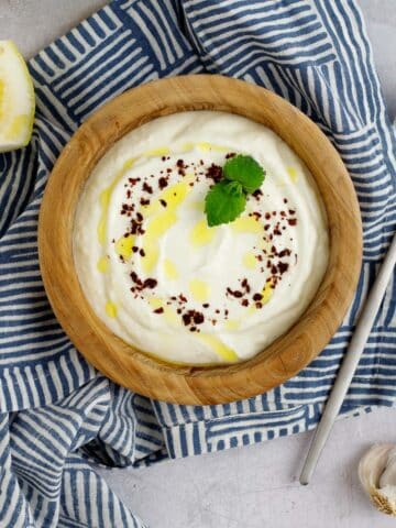 Lemon garlic yogurt sauce in a bowl garnished with sumac and mint.