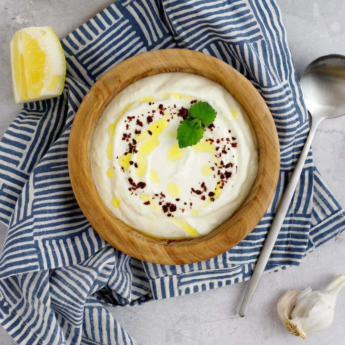 Lemon garlic yogurt sauce in a bowl garnished with sumac and mint.