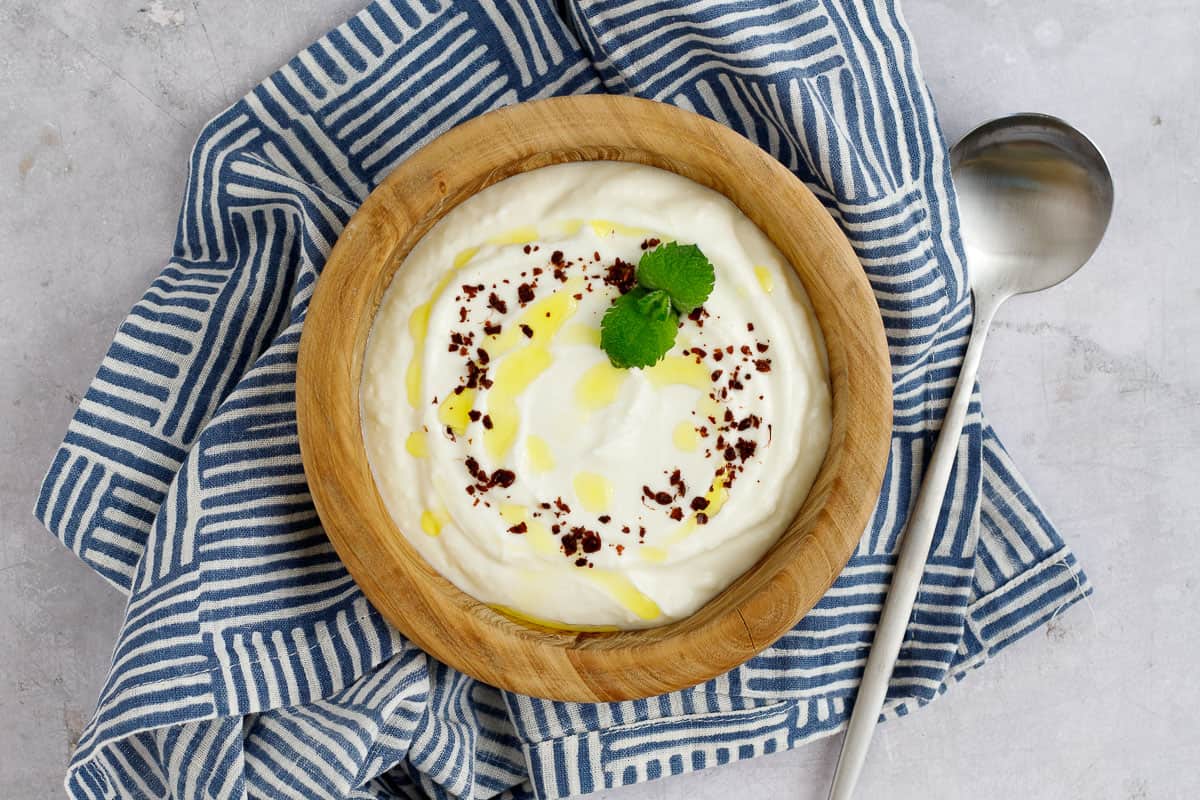 Lemon garlic yogurt sauce in a bowl garnished with sumac and mint.