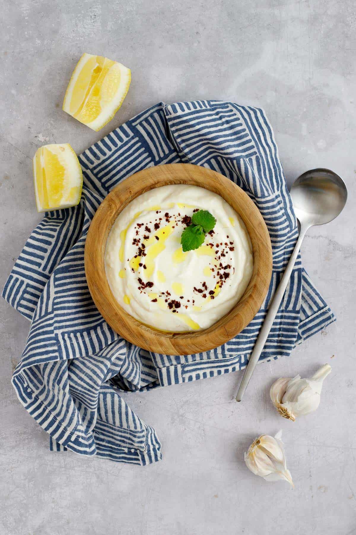 Lemon garlic yogurt sauce in a bowl garnished with sumac and mint.