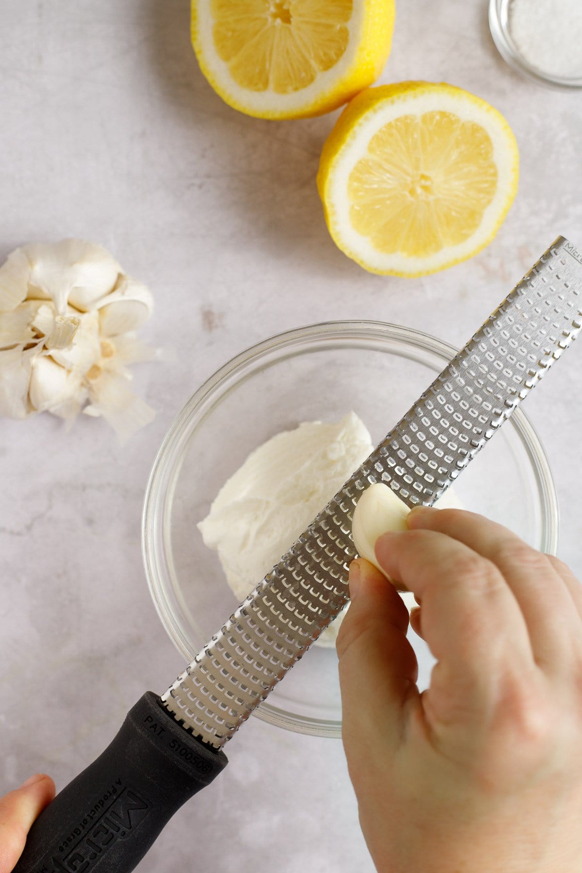 A person grating garlic into yogurt sauce using a rasp.