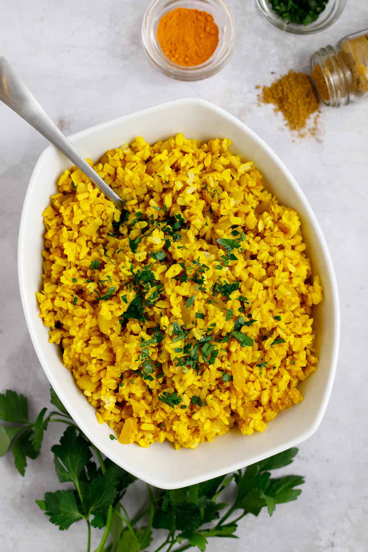 Mediterranean yellow rice in a bowl with a spoon. Garnished with parsley.