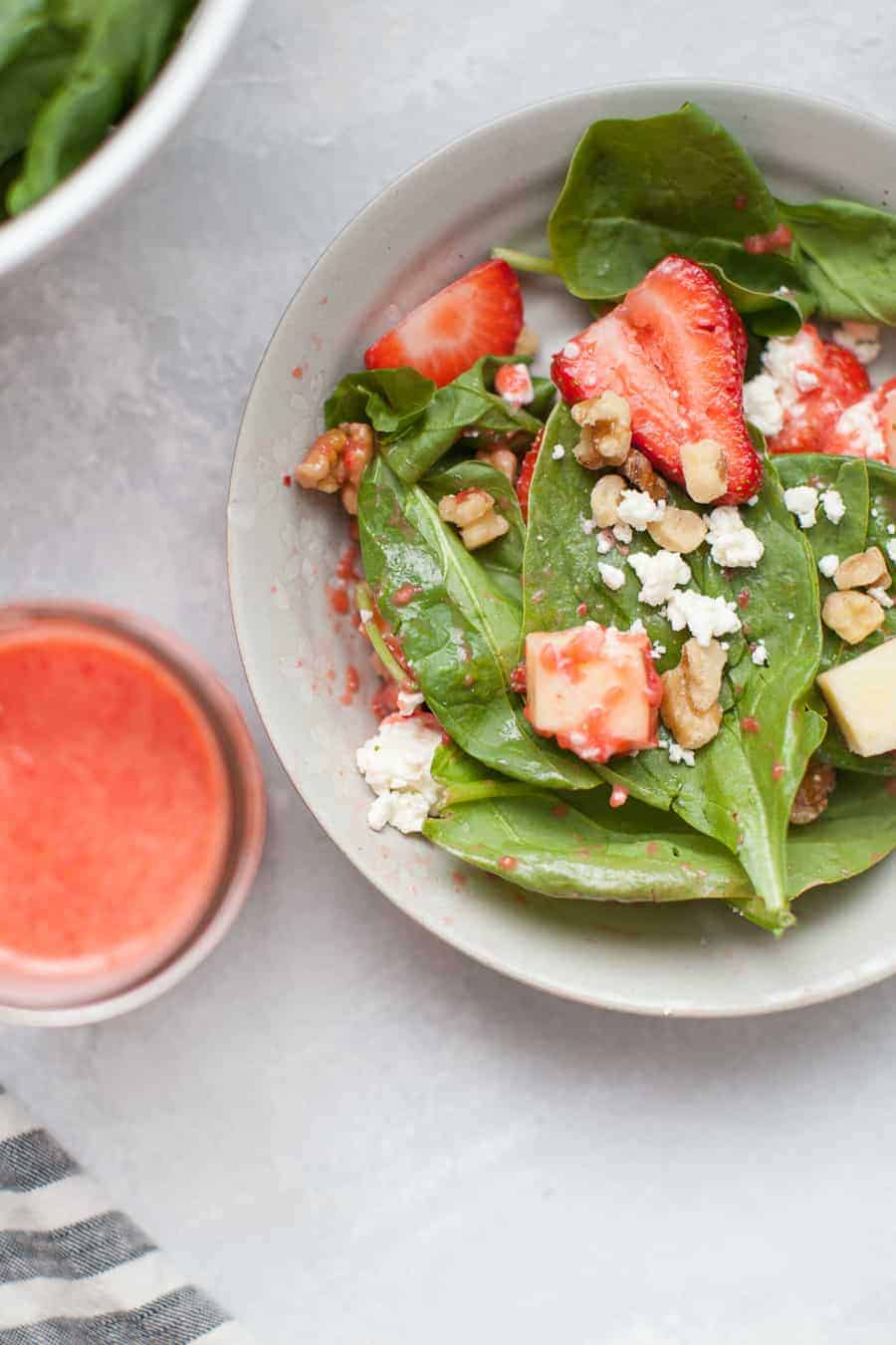 Strawberry spinach salad in a bowl with a small bowl of strawberry dressing nearby.