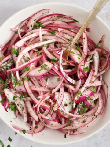 sumac pickled onions garnished with parsley in a bowl with a spoon.
