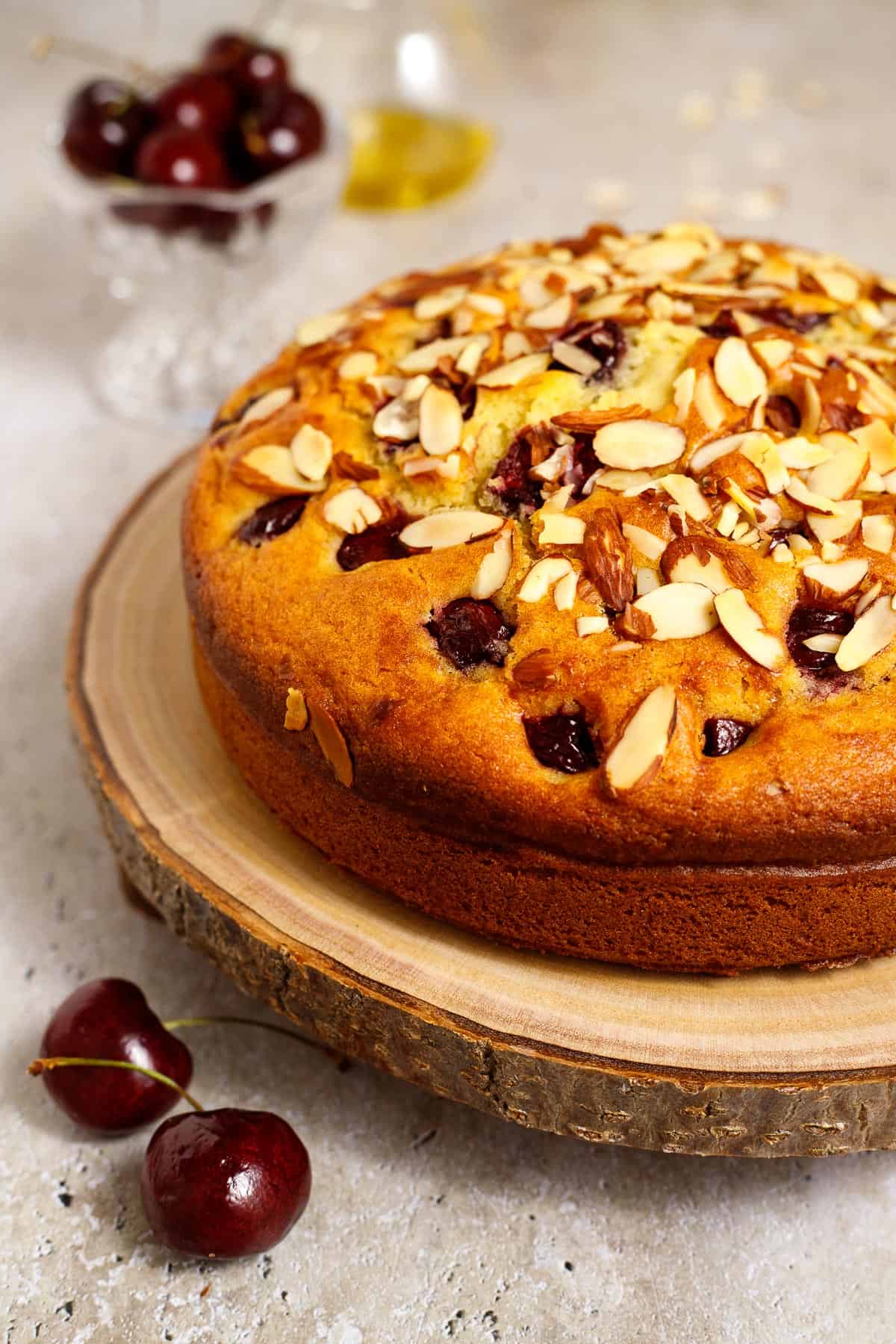 Cherry almond olive oil cake topped with sliced almonds, served on a wooden cake board.