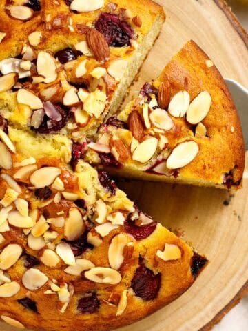olive oil cake with cherries and almonds on a wood cutting board.