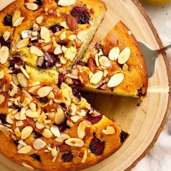 olive oil cake with cherries and almonds on a wood cutting board.