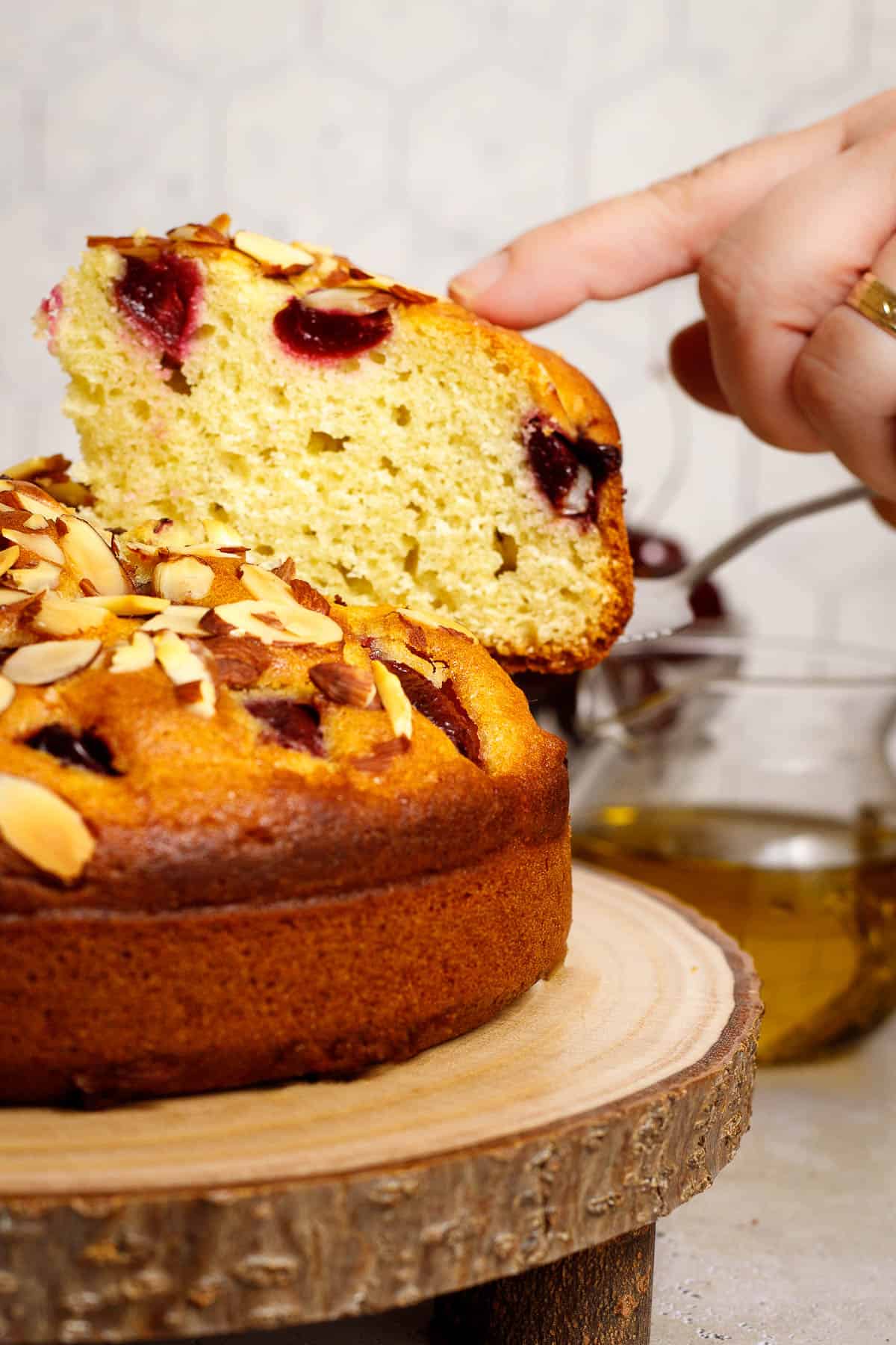 A slice of cherry almond olive oil cake is lifted with a spatula.