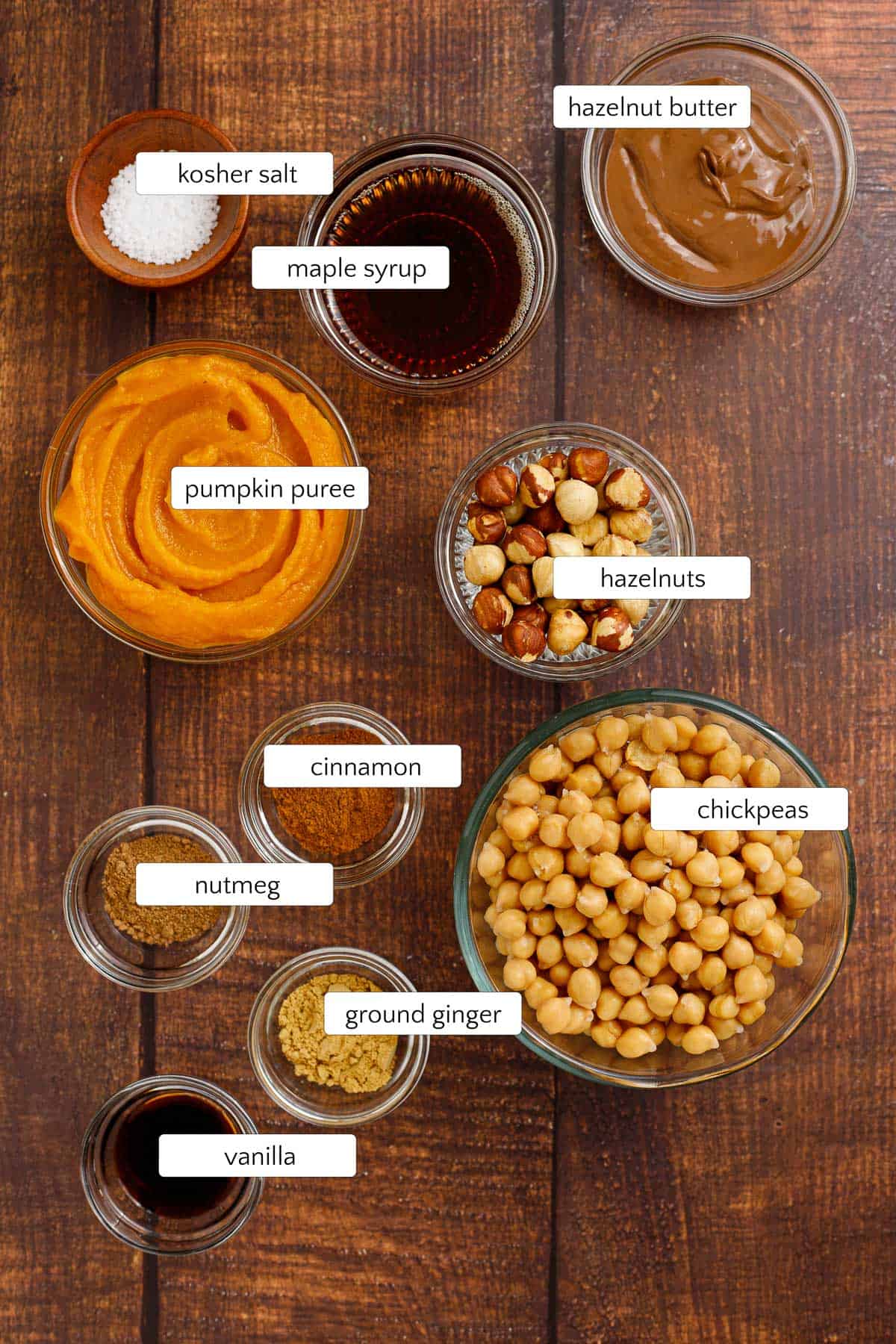 Ingredients for pumpkin dessert hummus include garbanzo beans/chickpeas, hazelnut butter, maple syrup, kosher salt, cinnamon, nutmeg, ground ginger, vanilla extract, and pumpkin puree. Toasted hazelnuts are optional for topping.