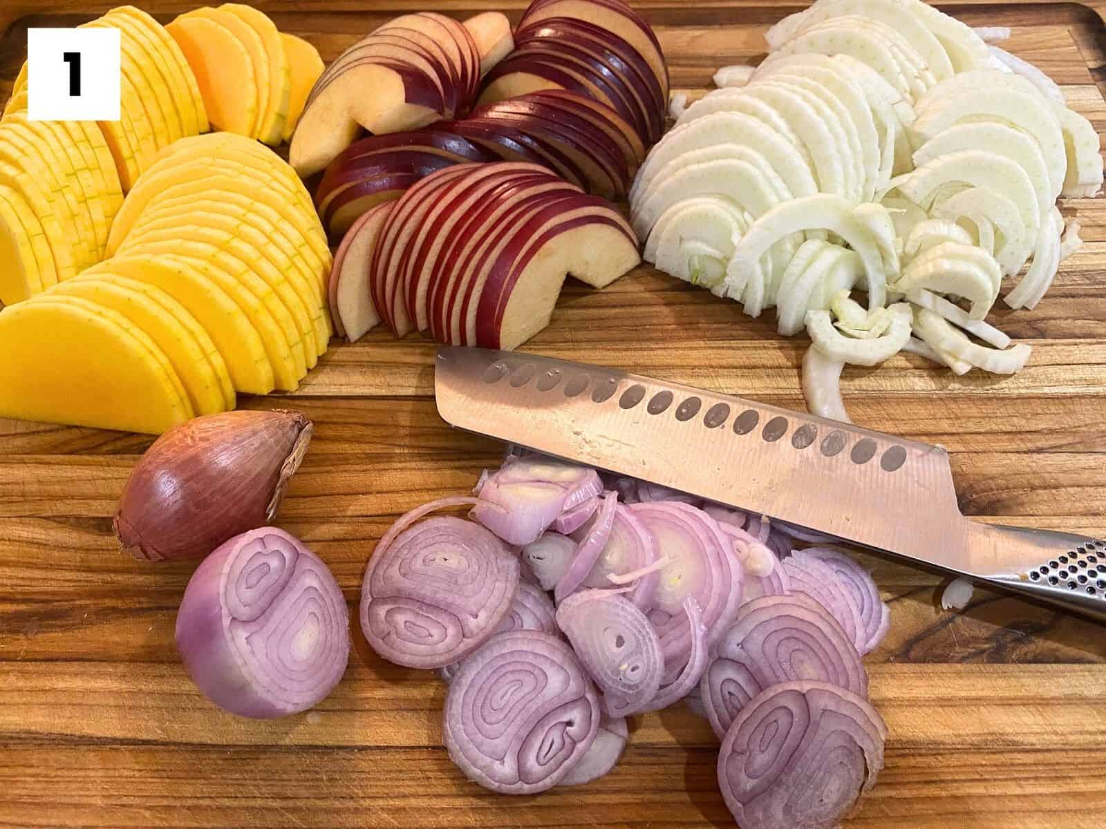 This image shows step one of this recipe. Sliced butternut squash, apples, fennel, and shallots sit on a cutting board with a knife.