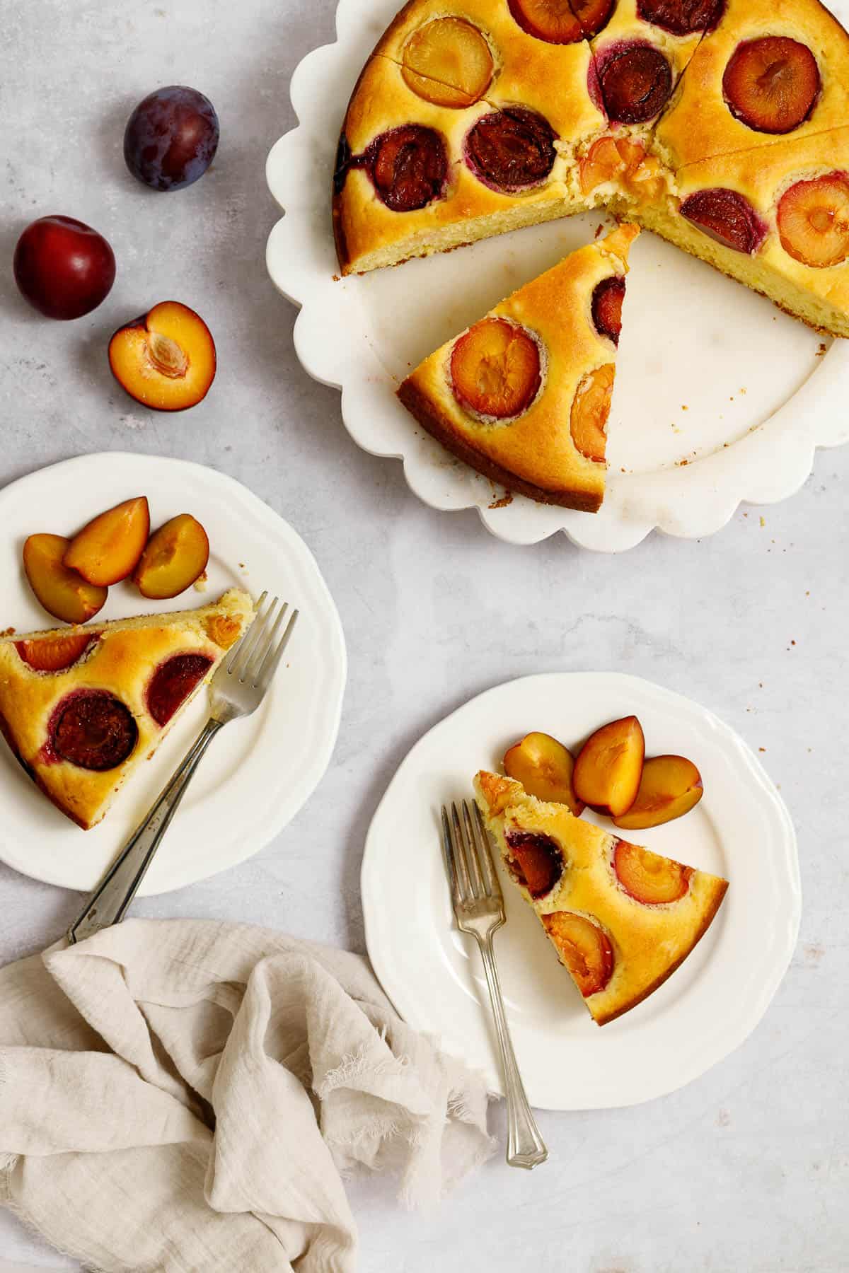 This image shows an olive oil cake that has been sliced and served. Two plates sit nearby with pieces of cake and forks. 