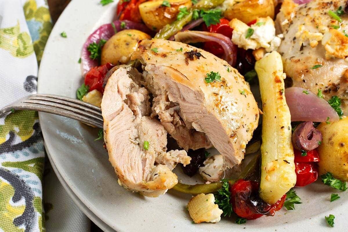 Greek chicken on a plate with olives, lemon, and vegetables.