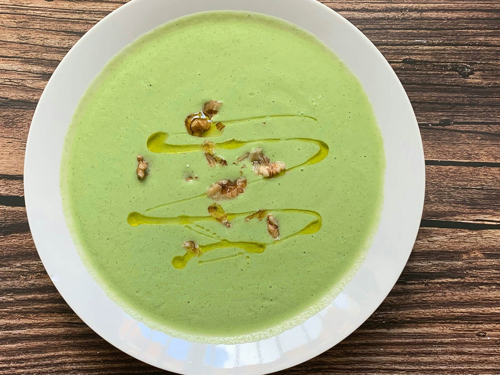 Blended green vegetable soup garnished with walnuts and drizzled with olive oil.