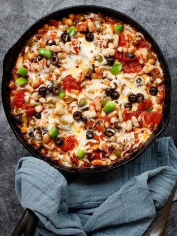 cheesy pizza beans in a cast iron pan with a spoon and a napkin