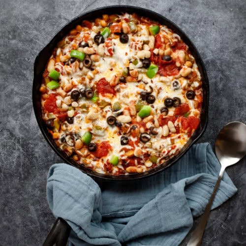 cheesy pizza beans in a cast iron pan with a spoon and a napkin