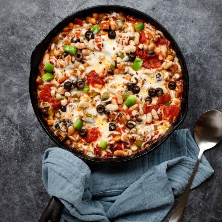 cheesy pizza beans in a cast iron pan with a spoon and a napkin