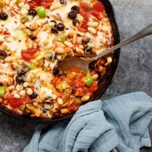 Skillet of cheesy pizza beans with a scoop taken out and a spoon.