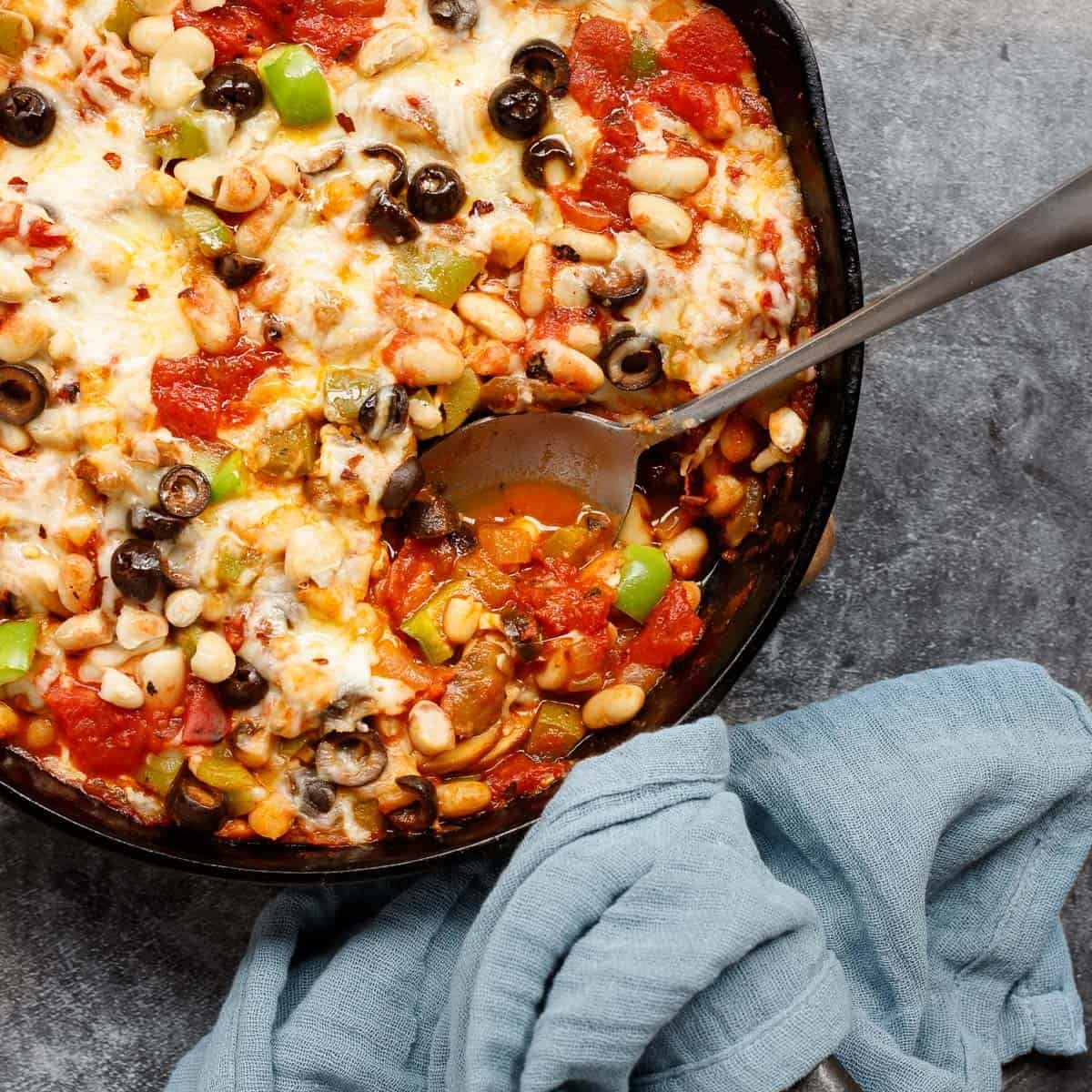 Skillet of cheesy pizza beans with a scoop taken out and a spoon.
