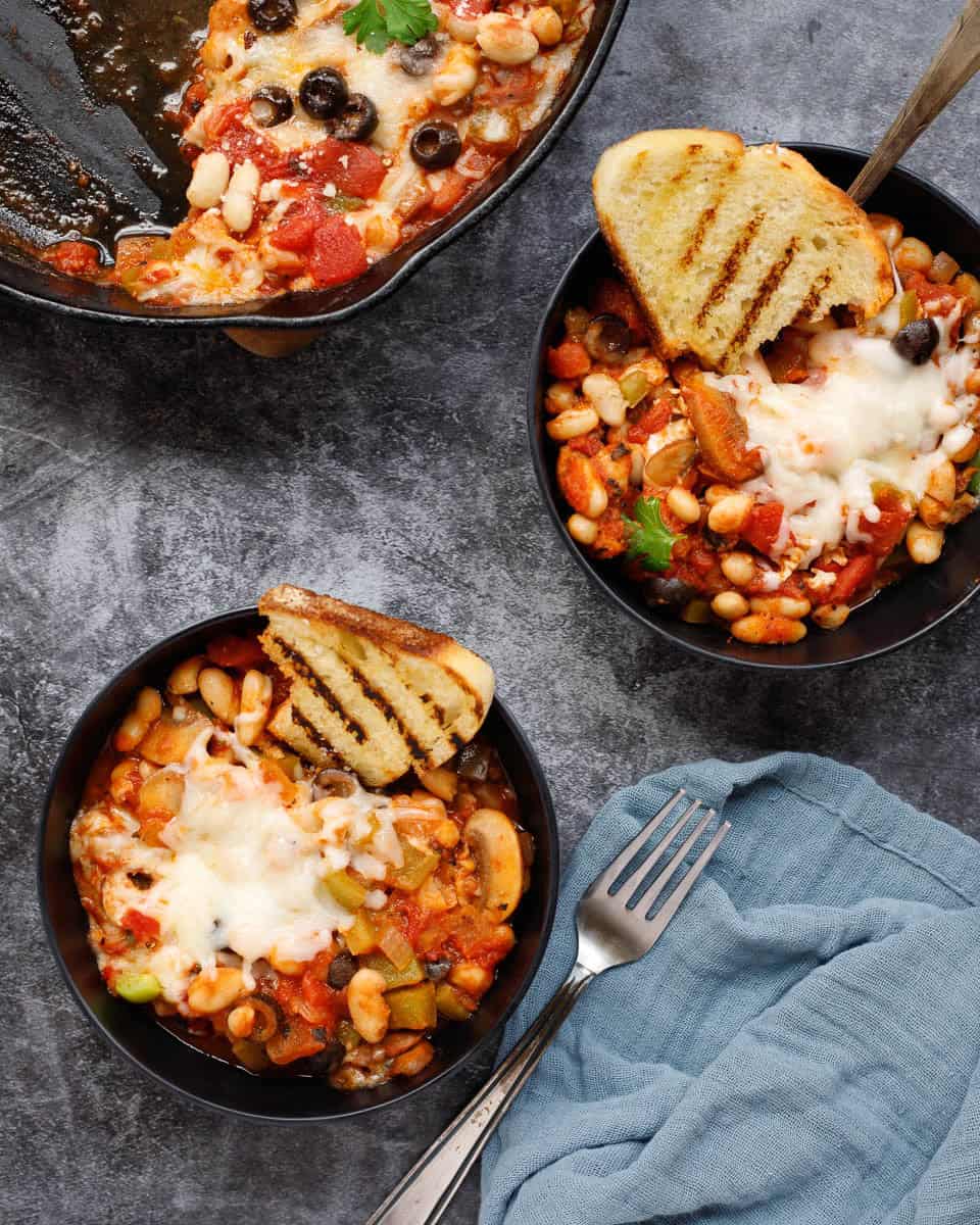 Two bowls of pizza beans with grilled bread and forks.