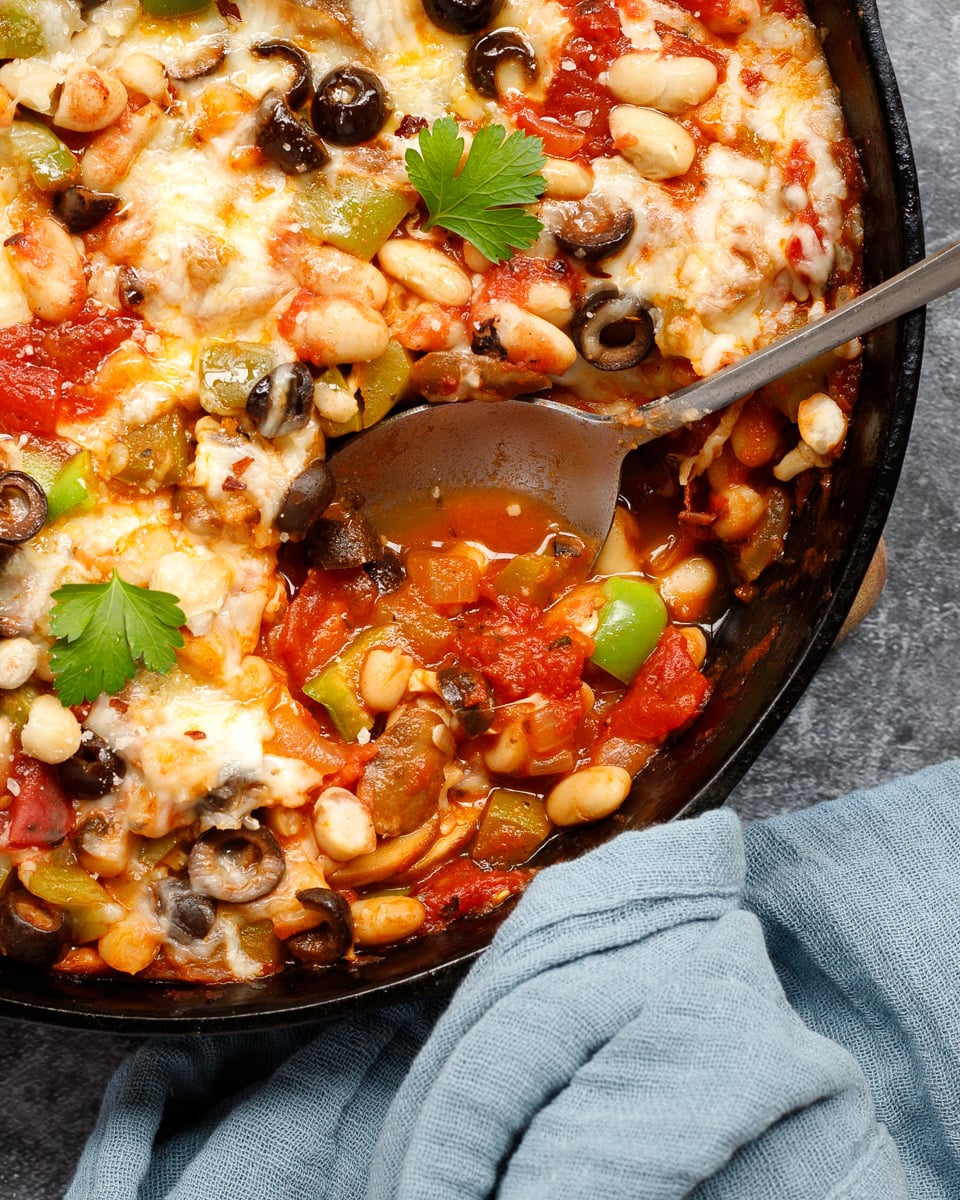 A skillet of pizza beans with a scoop taken out with a spoon and a napkin