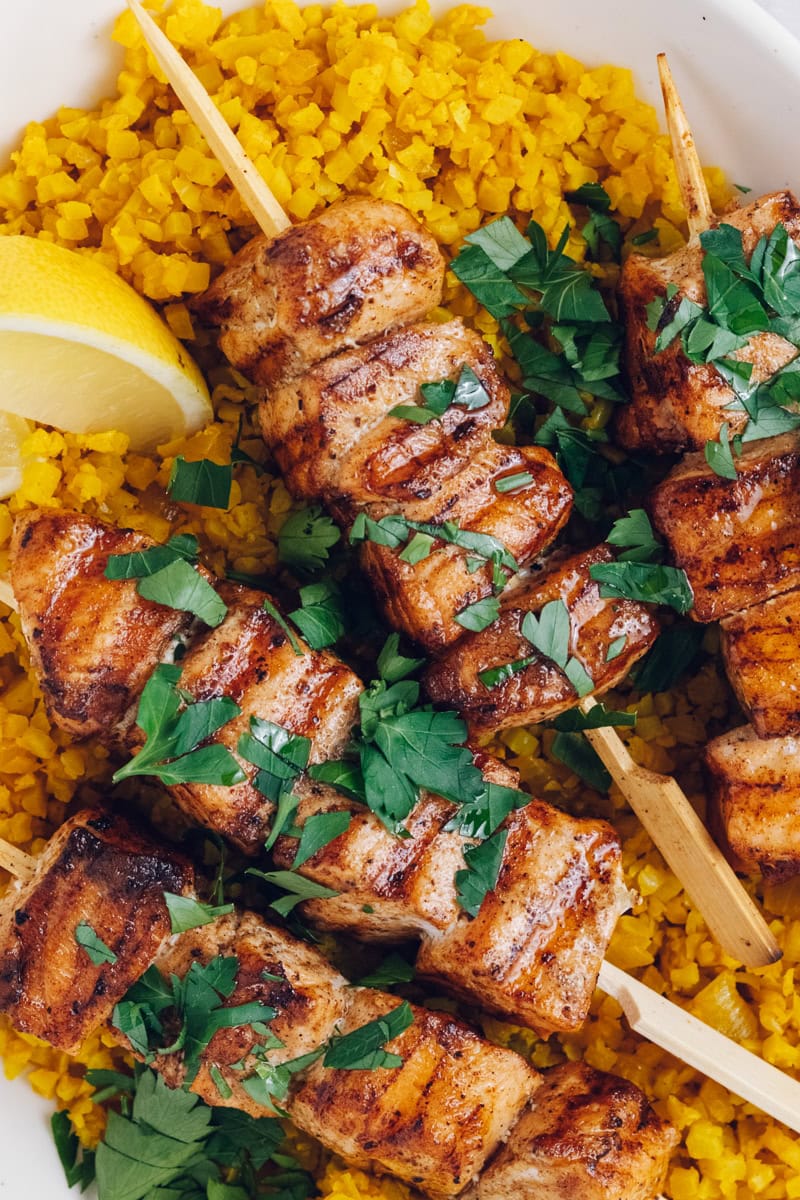 Grilled salmon skewers with shawarma seasoning on a bed of yellow cauliflower rice.
