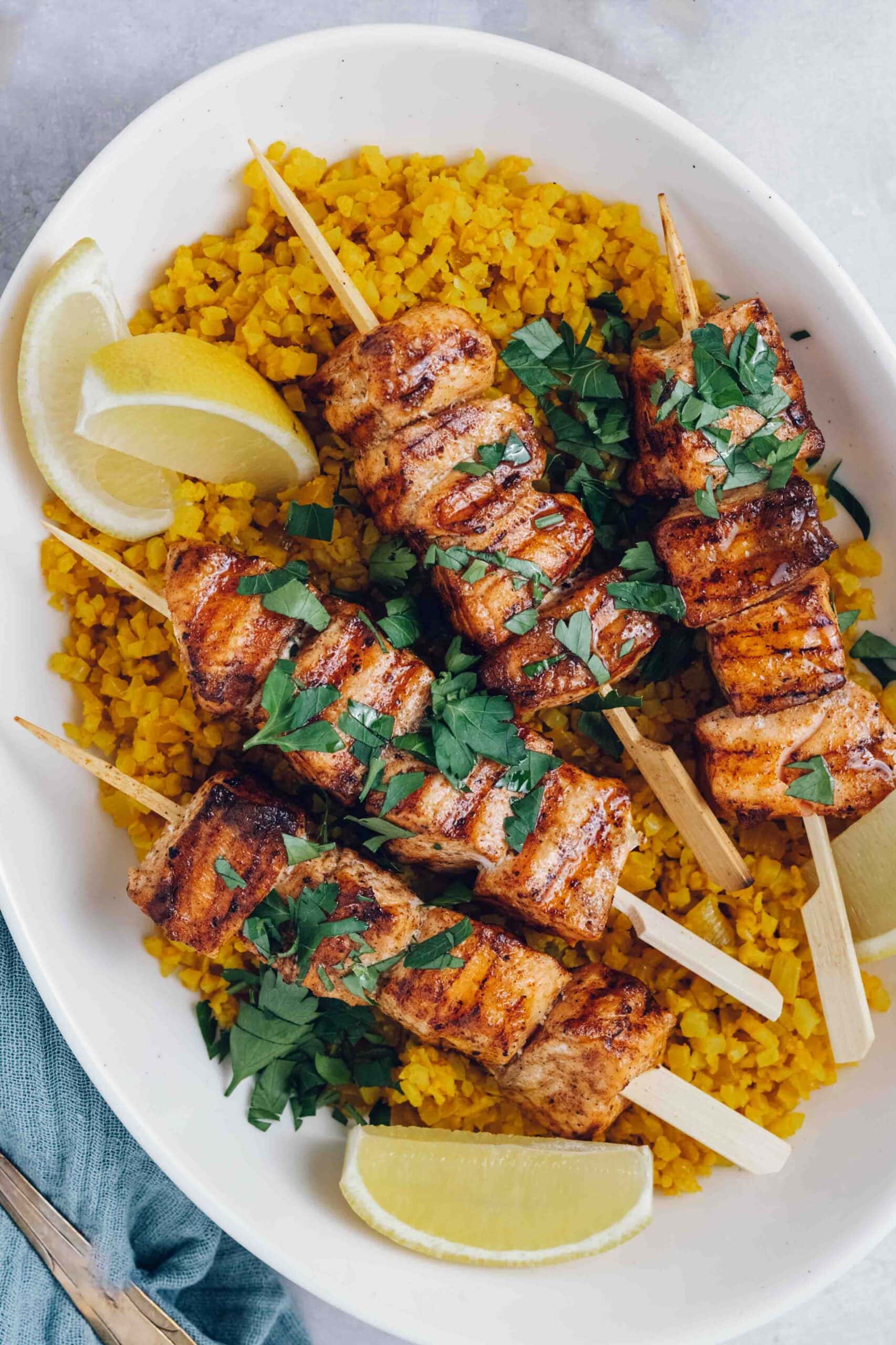 Grilled salmon kebabs on a bed of yellow cauliflower rice. Garnished with parsley and lemon wedges.