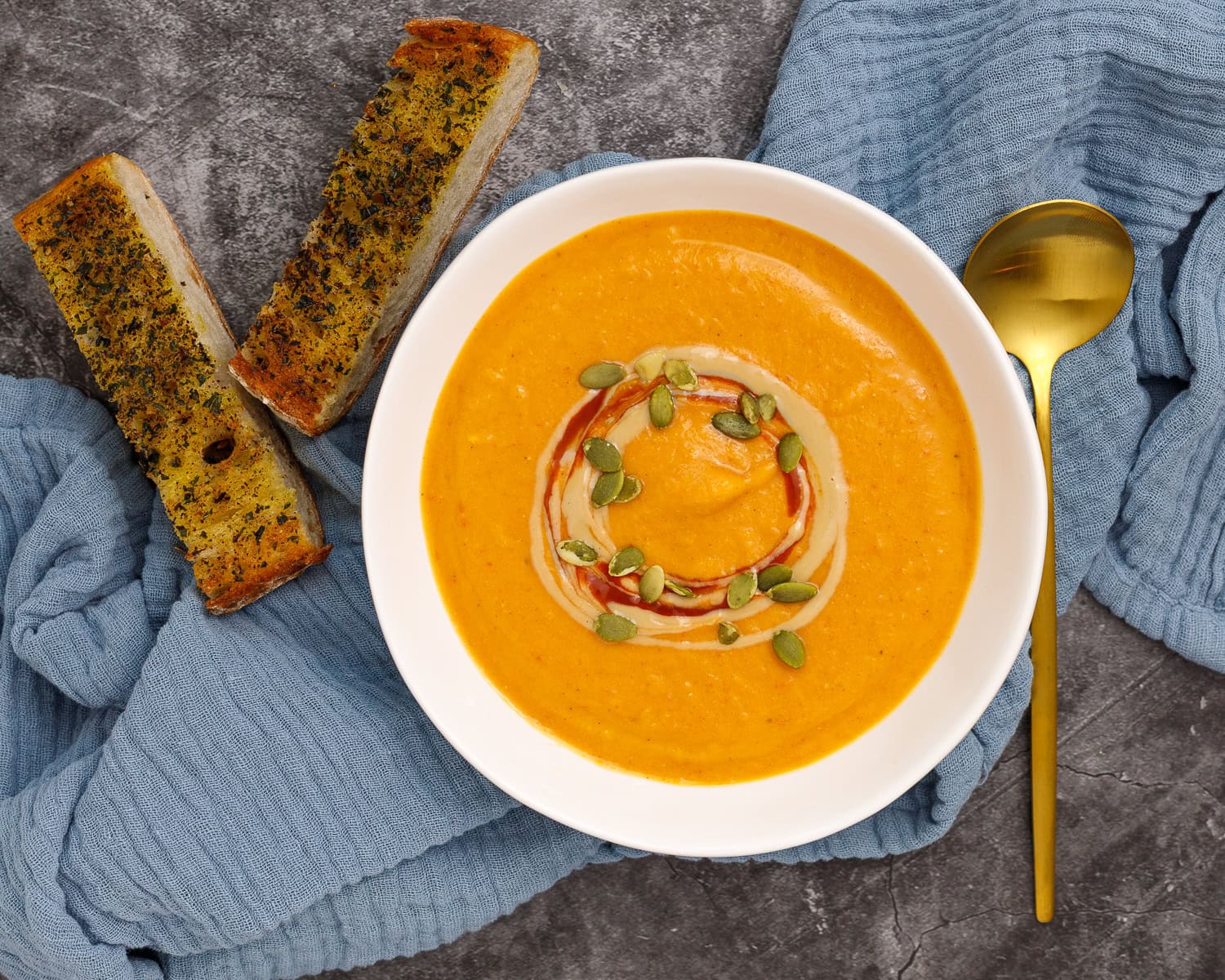 butternut squash and red pepper soup in a bowl with bread and a spoon.