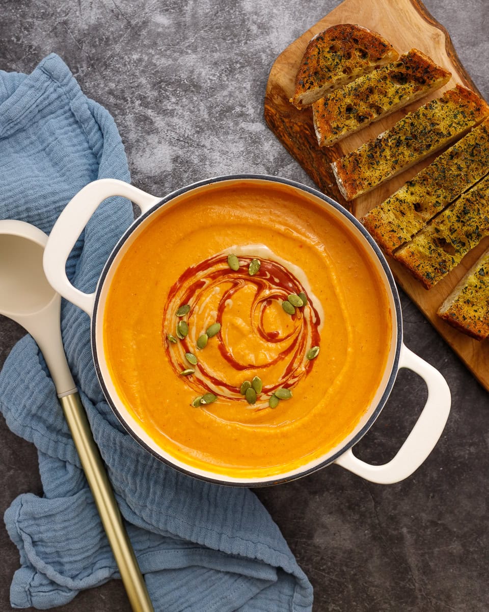 roasted butternut squash soup in a pot with a ladle sitting next to it. Toasted bread slices sit on a wood cutting board nearby.